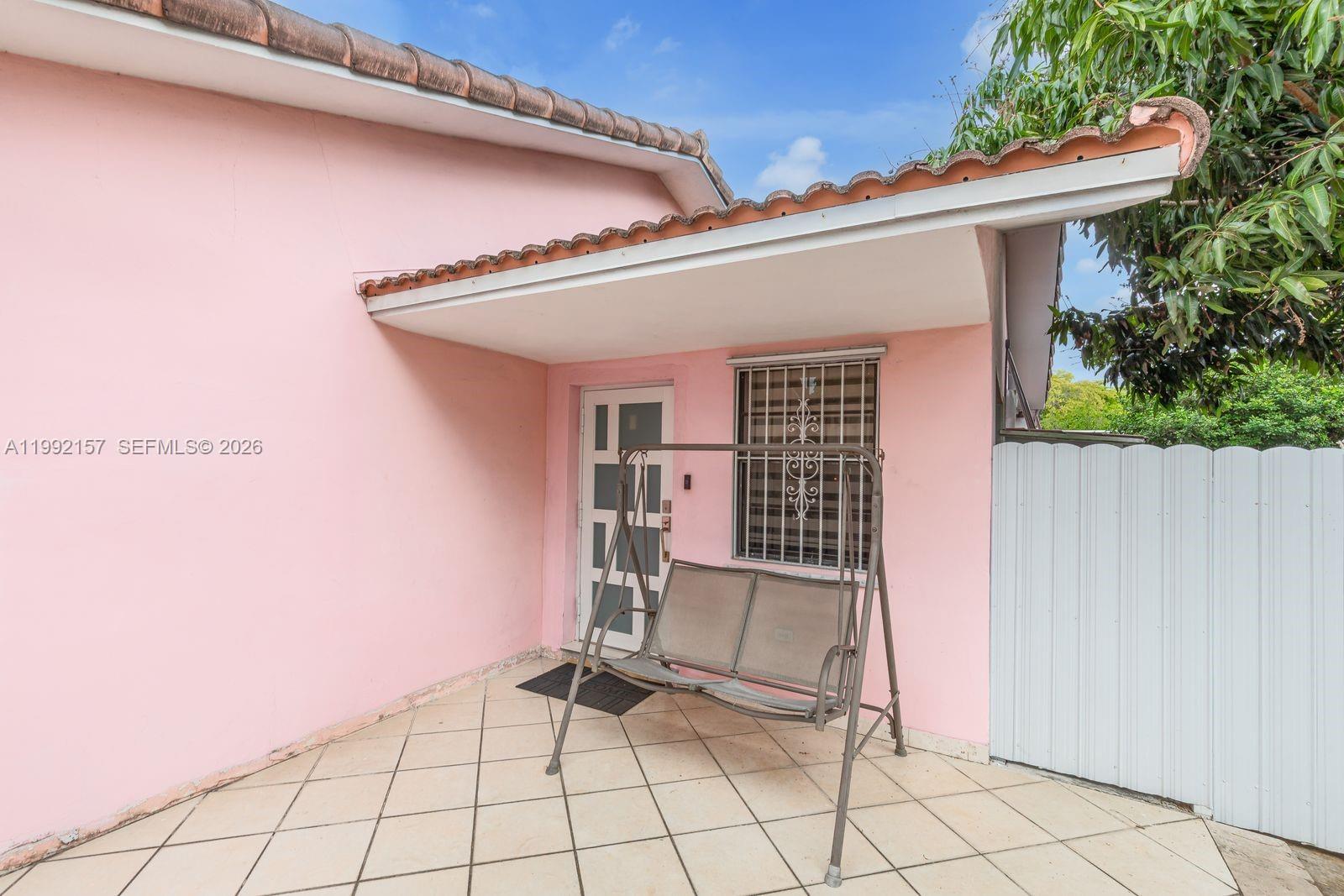 A pink exterior wall features a covered patio with a metal swing and tiled flooring — 1261 W 43rd Pl, Hialeah FL 33012, HIALEAH, FL