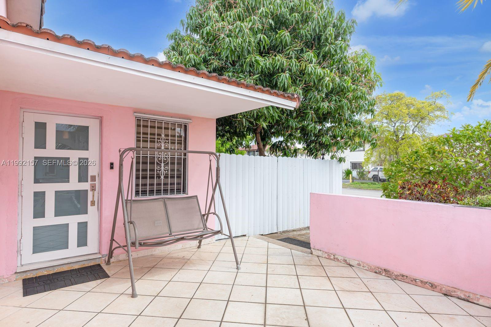 A pink exterior wall features a white door, a window with security bars, and a patio swing — 1261 W 43rd Pl, Hialeah FL 33012, HIALEAH, FL