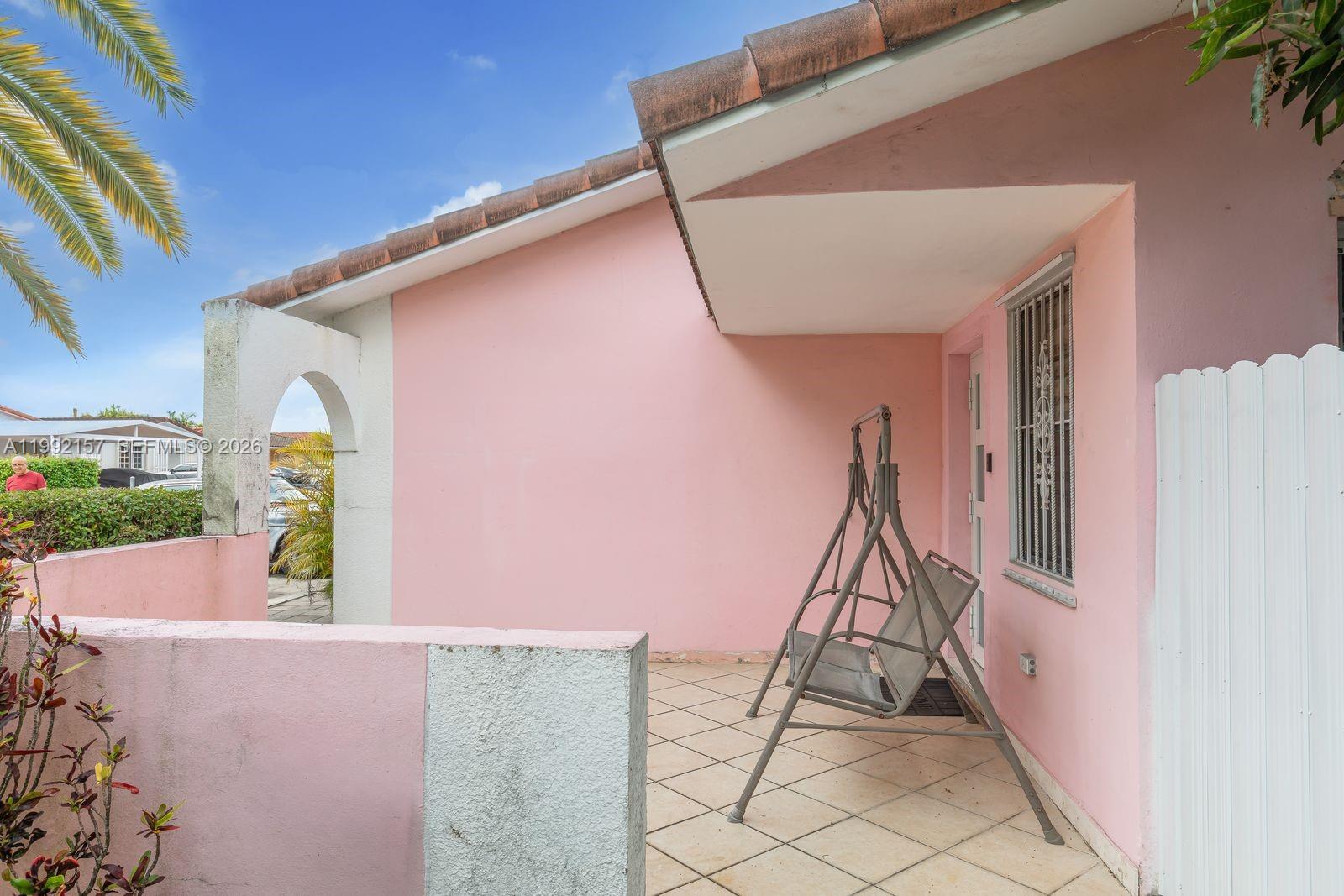 A pink exterior patio features a metal swing chair and tiled flooring under a roof — 1261 W 43rd Pl, Hialeah FL 33012, HIALEAH, FL