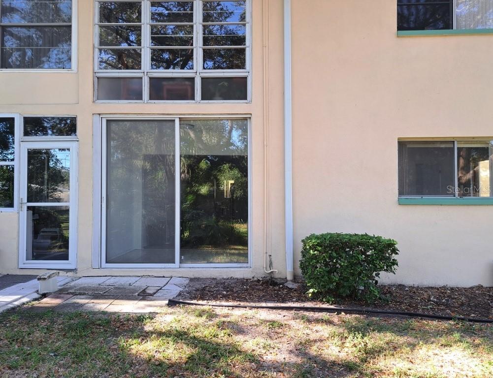 The exterior of a multi-story building features a sliding glass door and a small bush — 2005 GREENBRIAR BOULEVARD UNIT 1, CLEARWATER, FL
