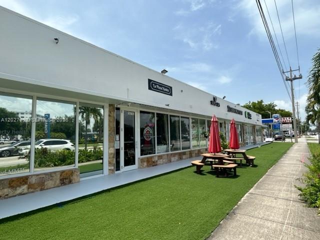 The exterior of a commercial strip mall features a storefront with outdoor seating on artificial turf — MIAMI, FL