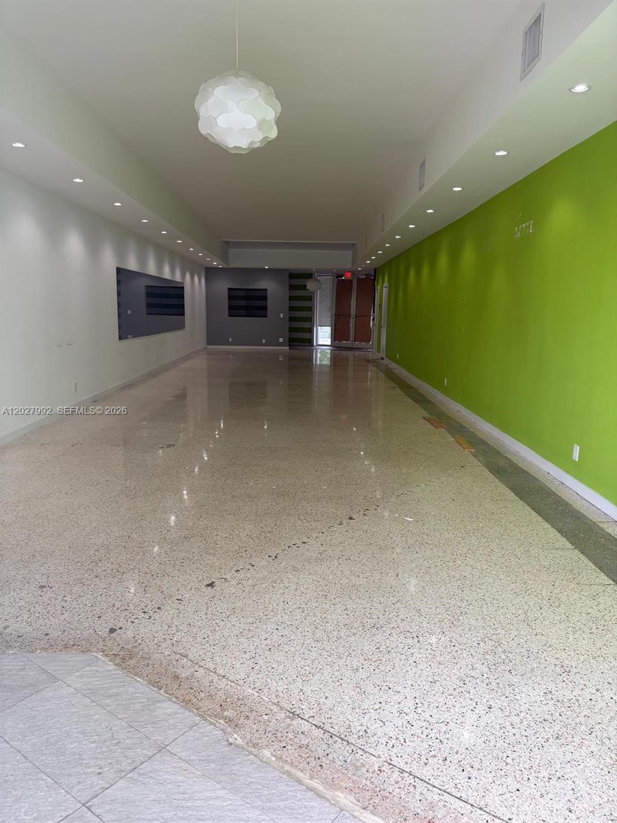 A long, narrow commercial space features polished terrazzo floors, recessed lighting, and lime green walls — MIAMI, FL