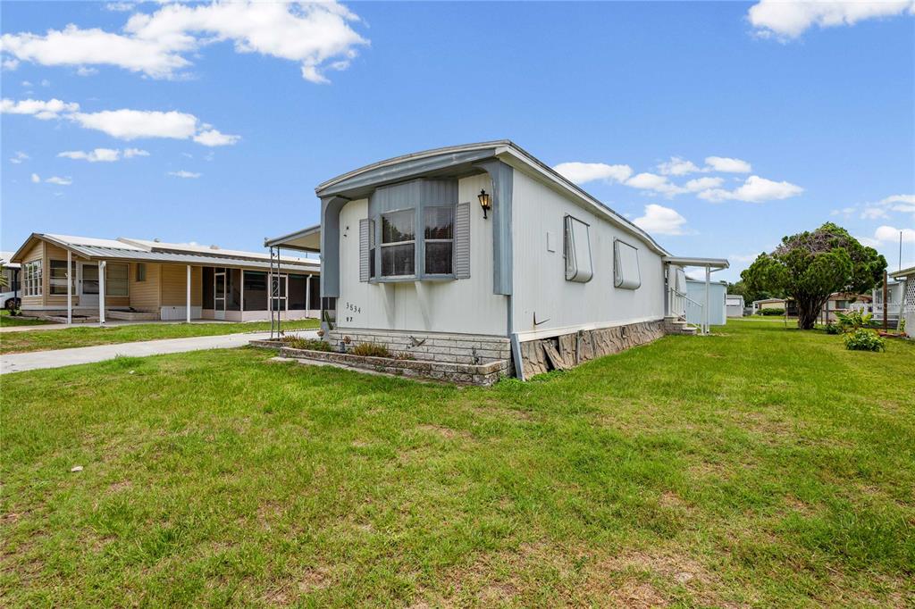 A white manufactured home with a bay window sits on a grassy lot — 3834 SARAH DRIVE, WESLEY CHAPEL, FL