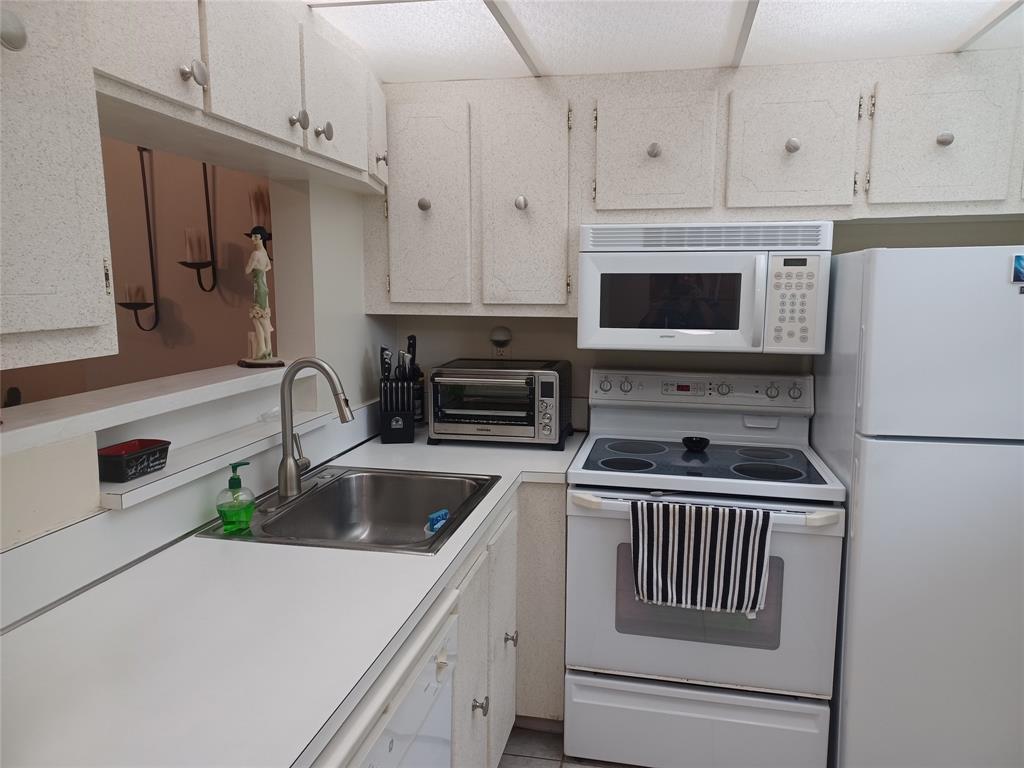 A kitchen features white cabinets, white appliances, a stainless steel sink, and a pass-through window — 1391 S Ocean Boulevard # 105, Pompano Beach FL 33062, POMPANO BEACH, FL