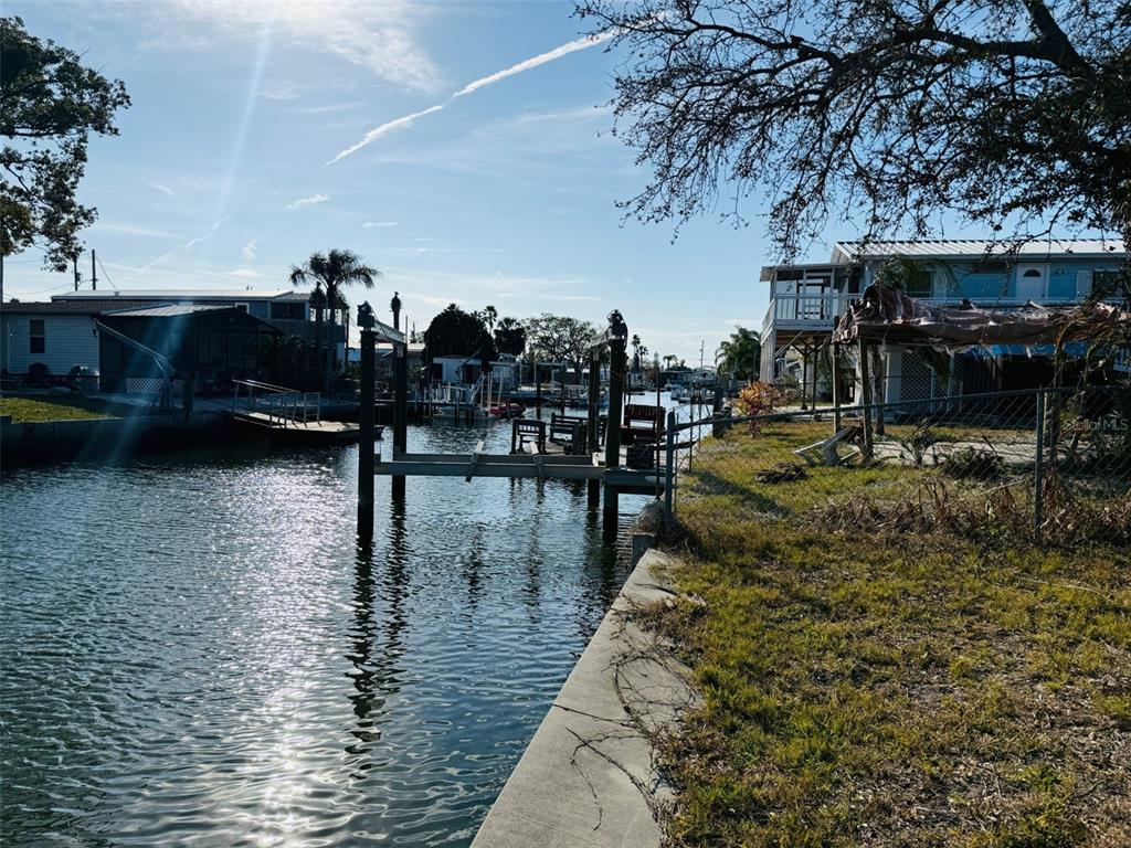 A canal view showing a boat lift, a concrete seawall, and nearby waterfront homes — 6822 GULL LANE, HUDSON, FL