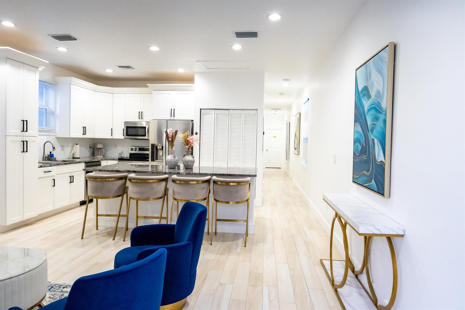 A modern kitchen features white cabinetry, a marble-topped island with four stools, and blue chairs — 214 N C Street, FL 33460, FL