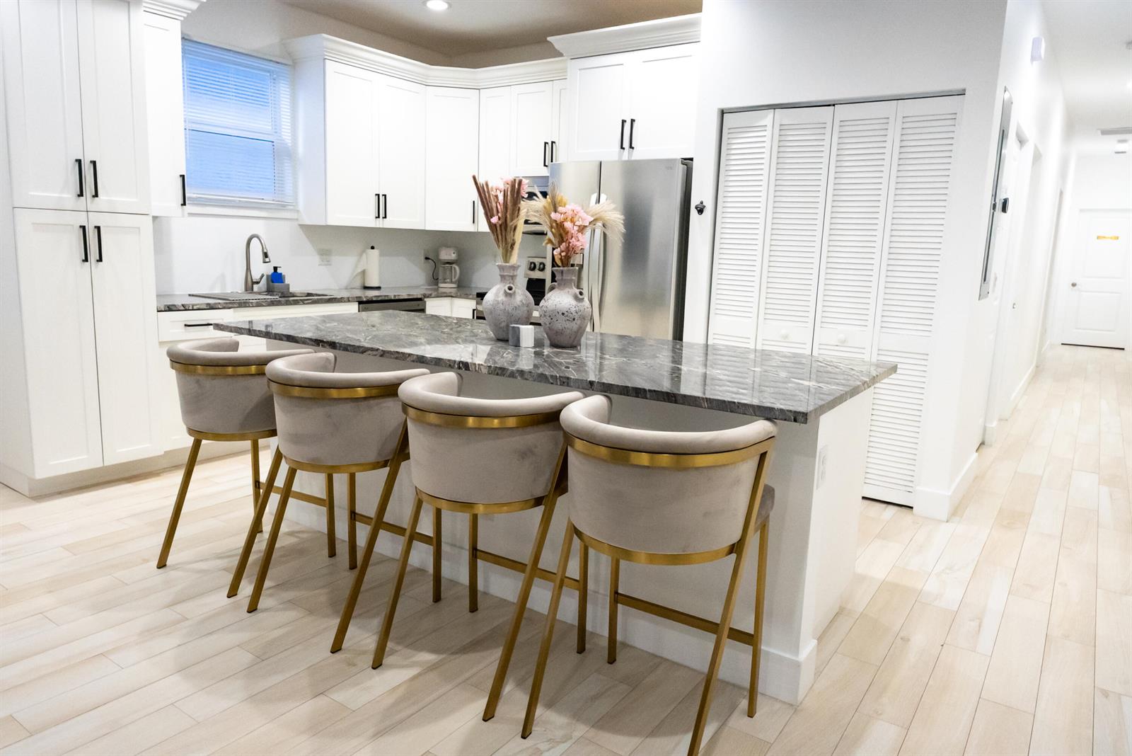 A modern kitchen features white cabinetry, a marble-topped island, and four velvet bar stools — 214 N C Street, FL 33460, FL