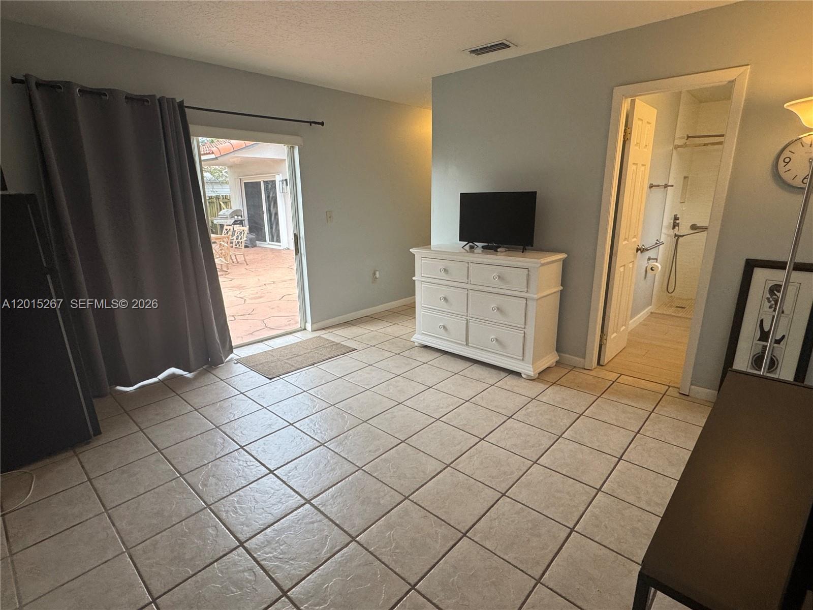 A room with tiled floors, a white dresser, a television, and a sliding glass door — 17016 SW 144th Ct # B, Miami FL 33177, MIAMI, FL