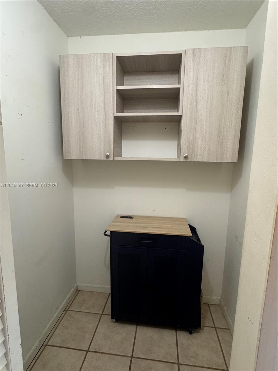 A small laundry or utility room features light wood-toned wall cabinets and a dark rolling cart — 17016 SW 144th Ct # B, Miami FL 33177, MIAMI, FL