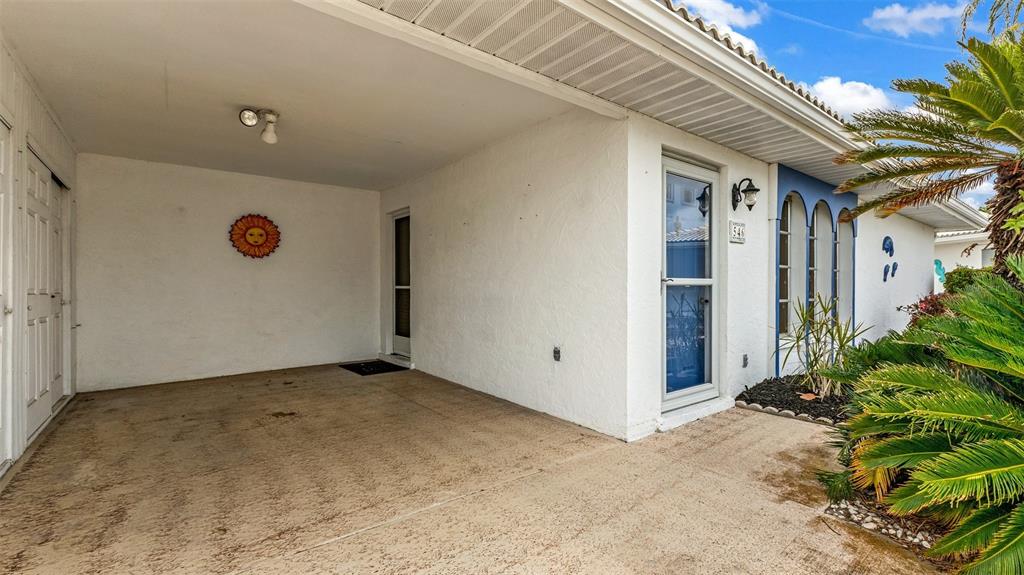 A covered concrete patio area features a white stucco wall, a sun decoration, and doors — 546 CIRCLEWOOD DRIVE UNIT P3-4, VENICE, FL