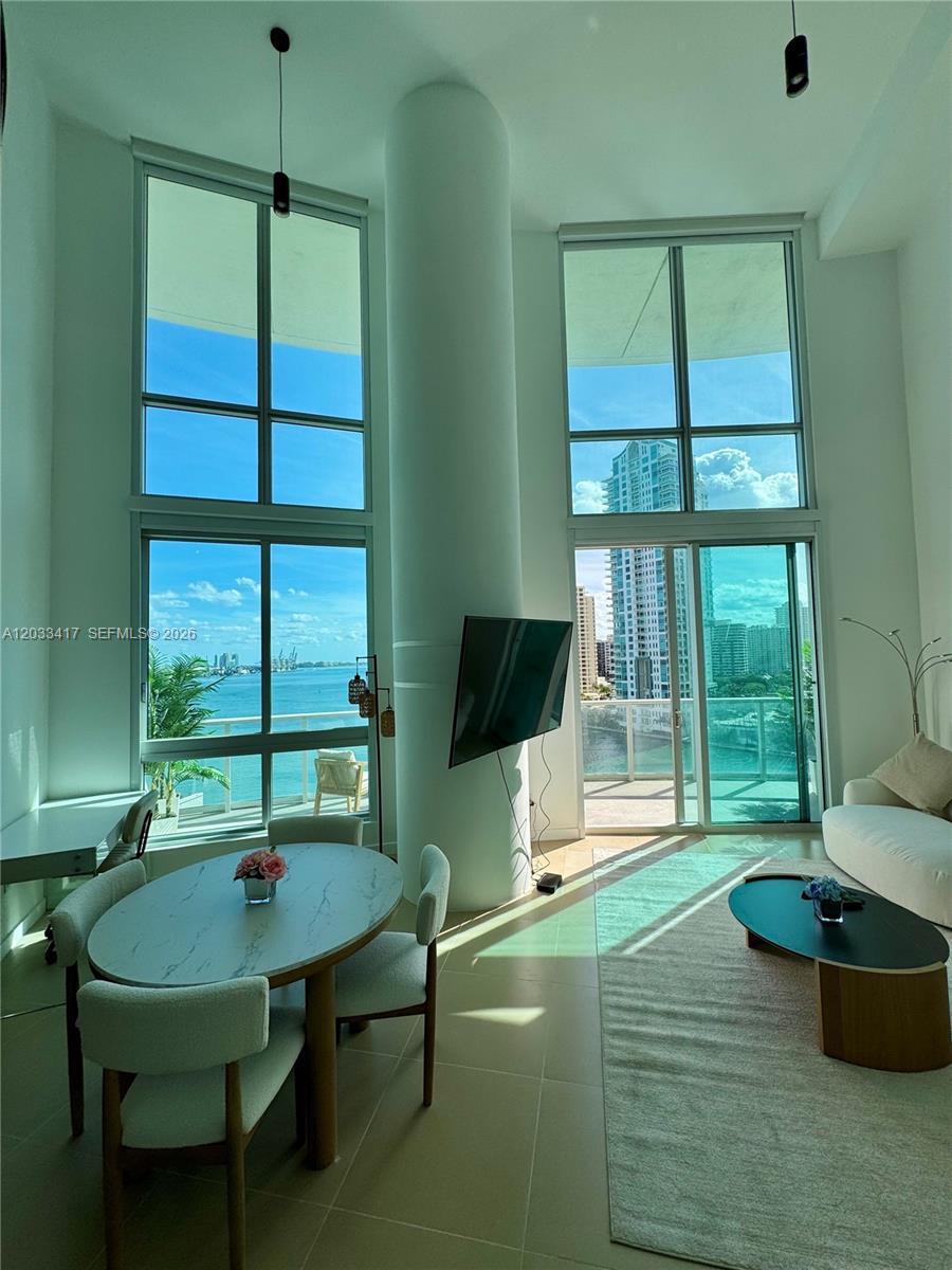 A modern living and dining area features floor-to-ceiling windows with views of the water — 300 S Biscayne Blvd # 1218, Miami FL 33131, MIAMI, FL