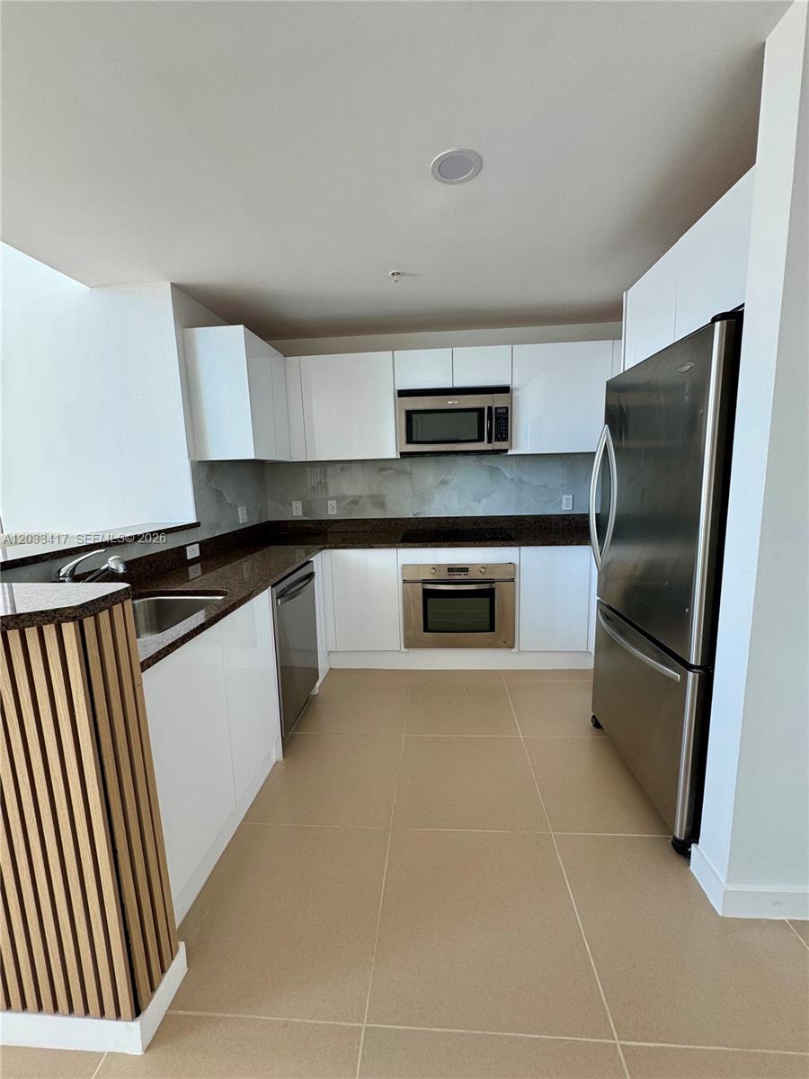 A modern kitchen features white cabinets, stainless steel appliances, and dark granite countertops — 300 S Biscayne Blvd # 1218, Miami FL 33131, MIAMI, FL
