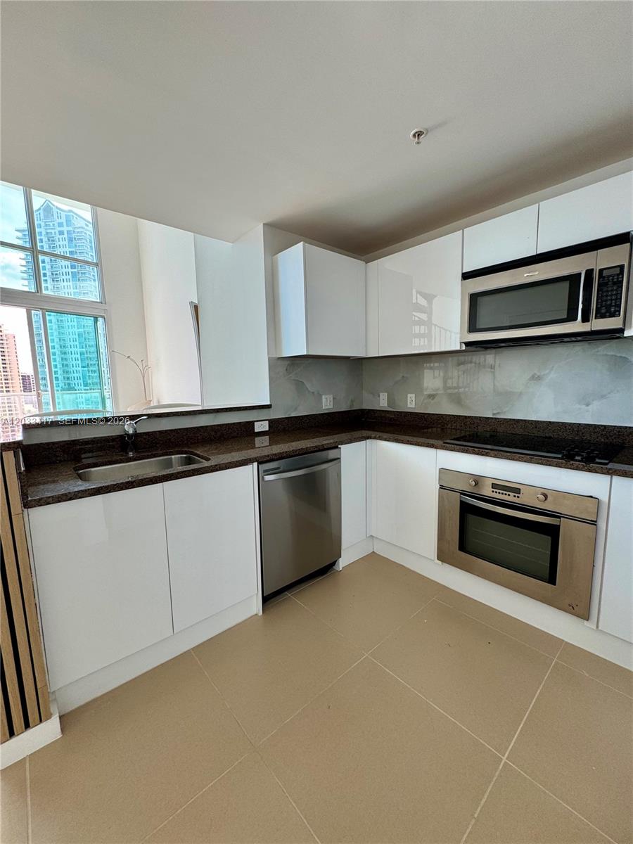 A modern kitchen features white cabinets, dark granite countertops, stainless steel appliances, and large windows — 300 S Biscayne Blvd # 1218, Miami FL 33131, MIAMI, FL