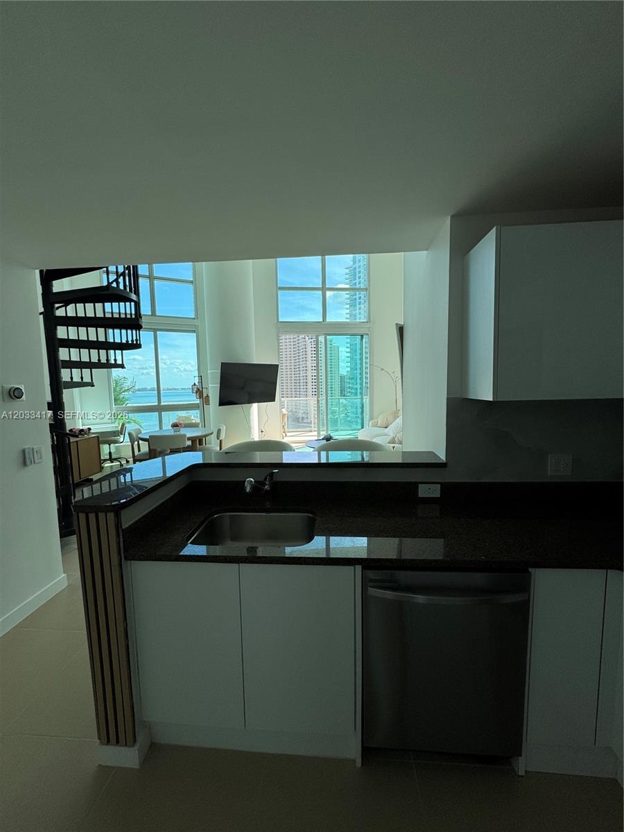 A kitchen with dark countertops and white cabinets overlooks a living area with floor-to-ceiling windows — 300 S Biscayne Blvd # 1218, Miami FL 33131, MIAMI, FL
