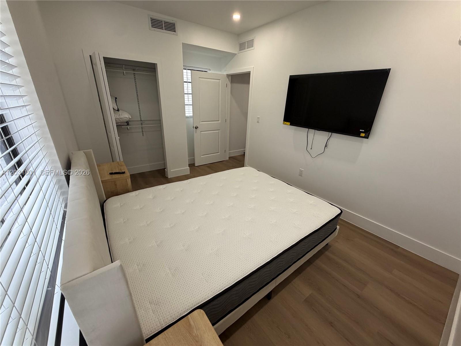 A bedroom features a mattress on a bed frame, a wall-mounted television, and wood flooring — 1619 Jefferson Ave # 210, Miami Beach FL 33139, MIAMI BEACH, FL