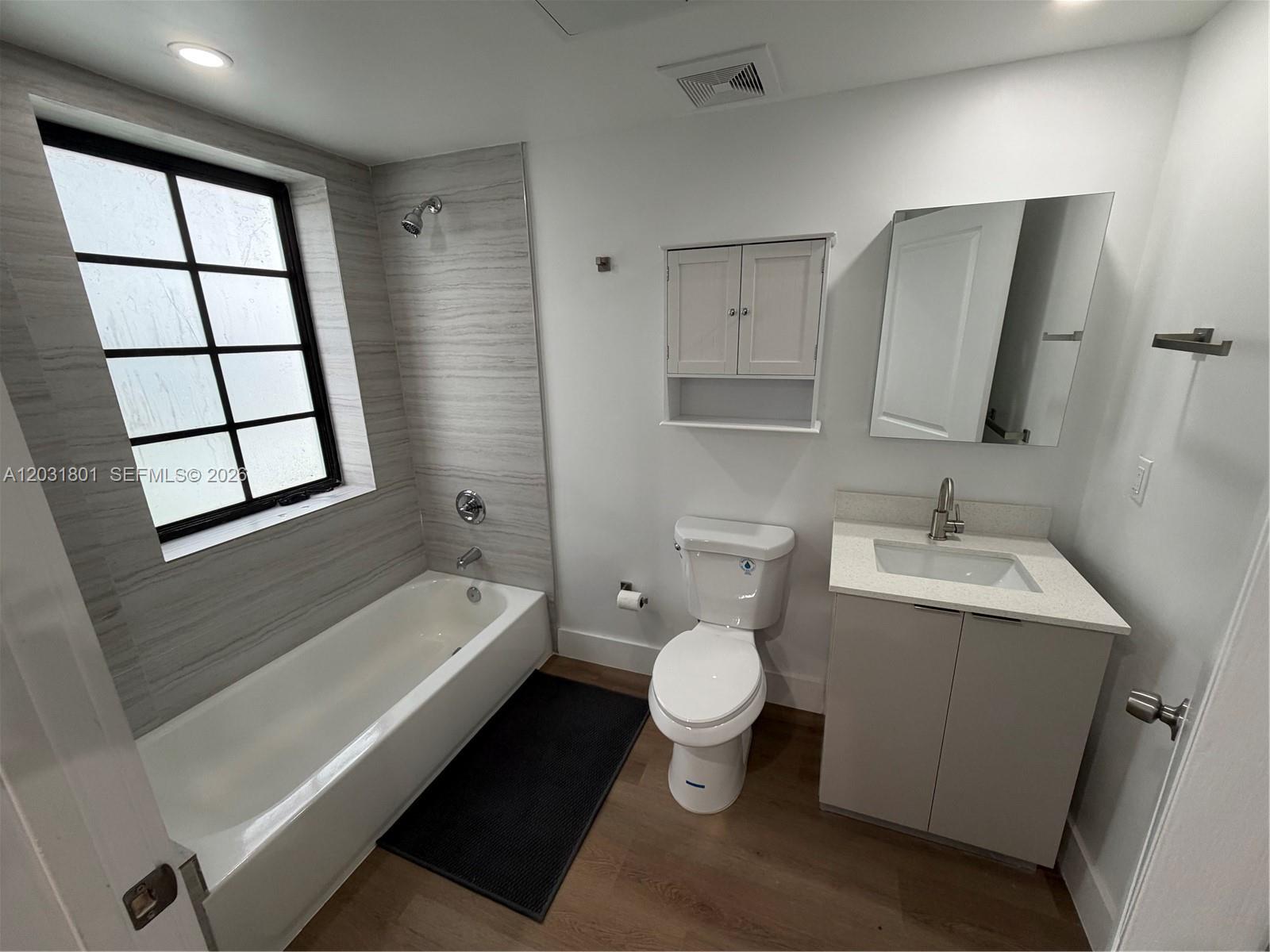 A bathroom features a bathtub with a shower, a toilet, and a vanity with mirror — 1619 Jefferson Ave # 210, Miami Beach FL 33139, MIAMI BEACH, FL