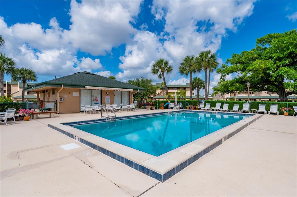A rectangular swimming pool sits on a concrete patio next to a clubhouse building — 601 SHREVE STREET UNIT 62C, PUNTA GORDA, FL