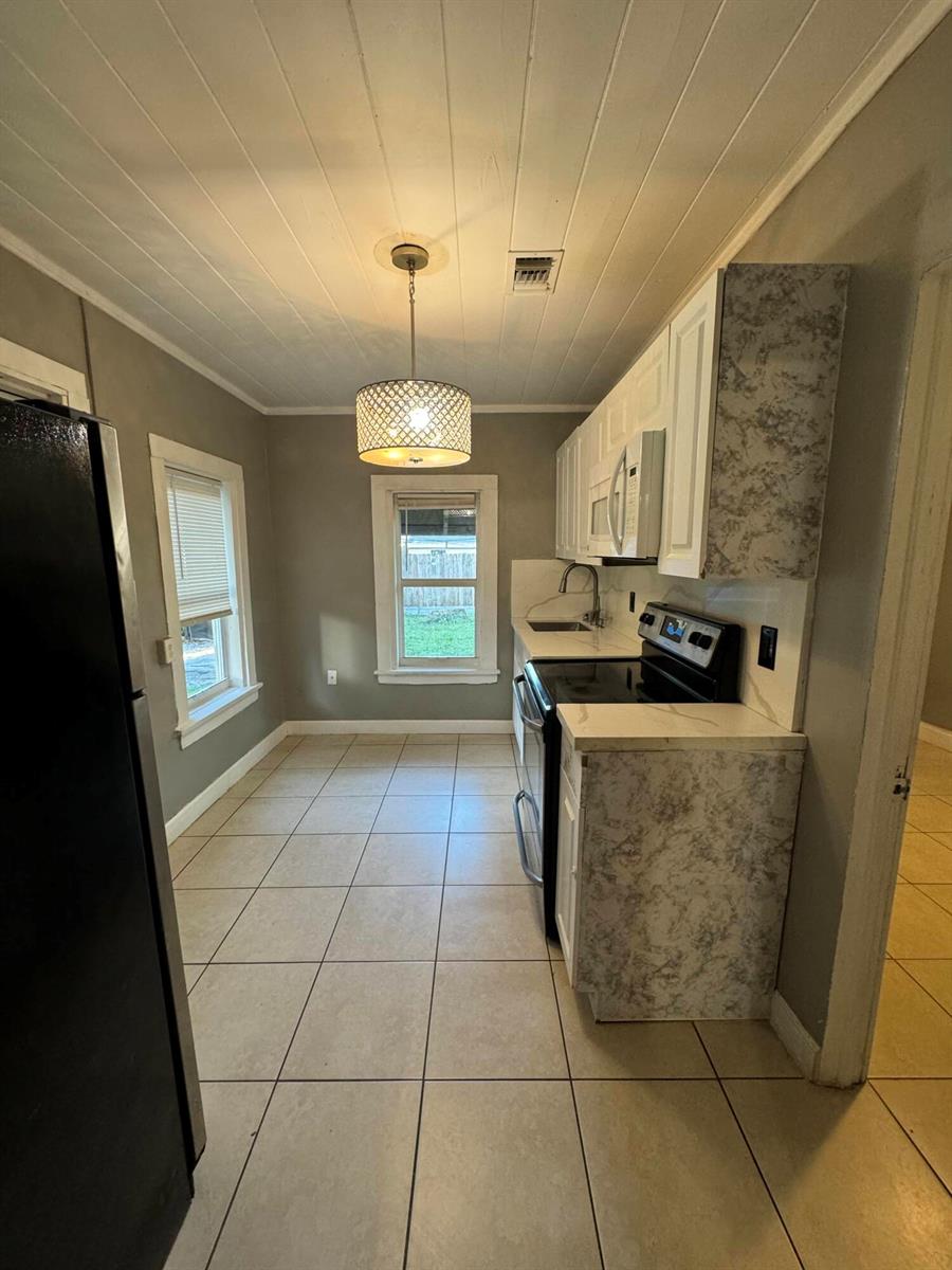 A kitchen features white cabinets, a black stove, tile flooring, and a hanging pendant light — 717 S B Street # 715, FL 33460, FL