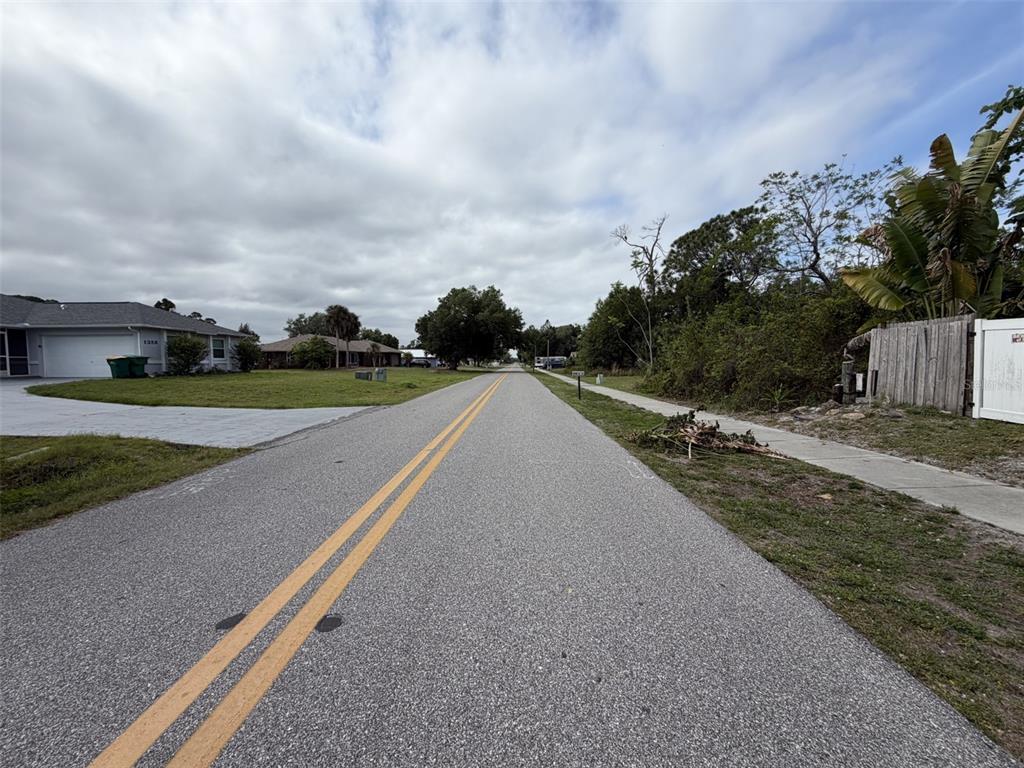 A paved residential street with double yellow lines stretches toward houses under a cloudy sky — 1352 ABALOM STREET, PORT CHARLOTTE, FL