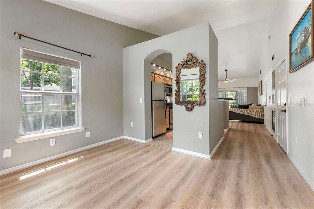 A dining area with light wood-look flooring, a window, and an arched entryway to the kitchen — 3638 TRAFALGAR WAY UNIT 101, PALM HARBOR, FL