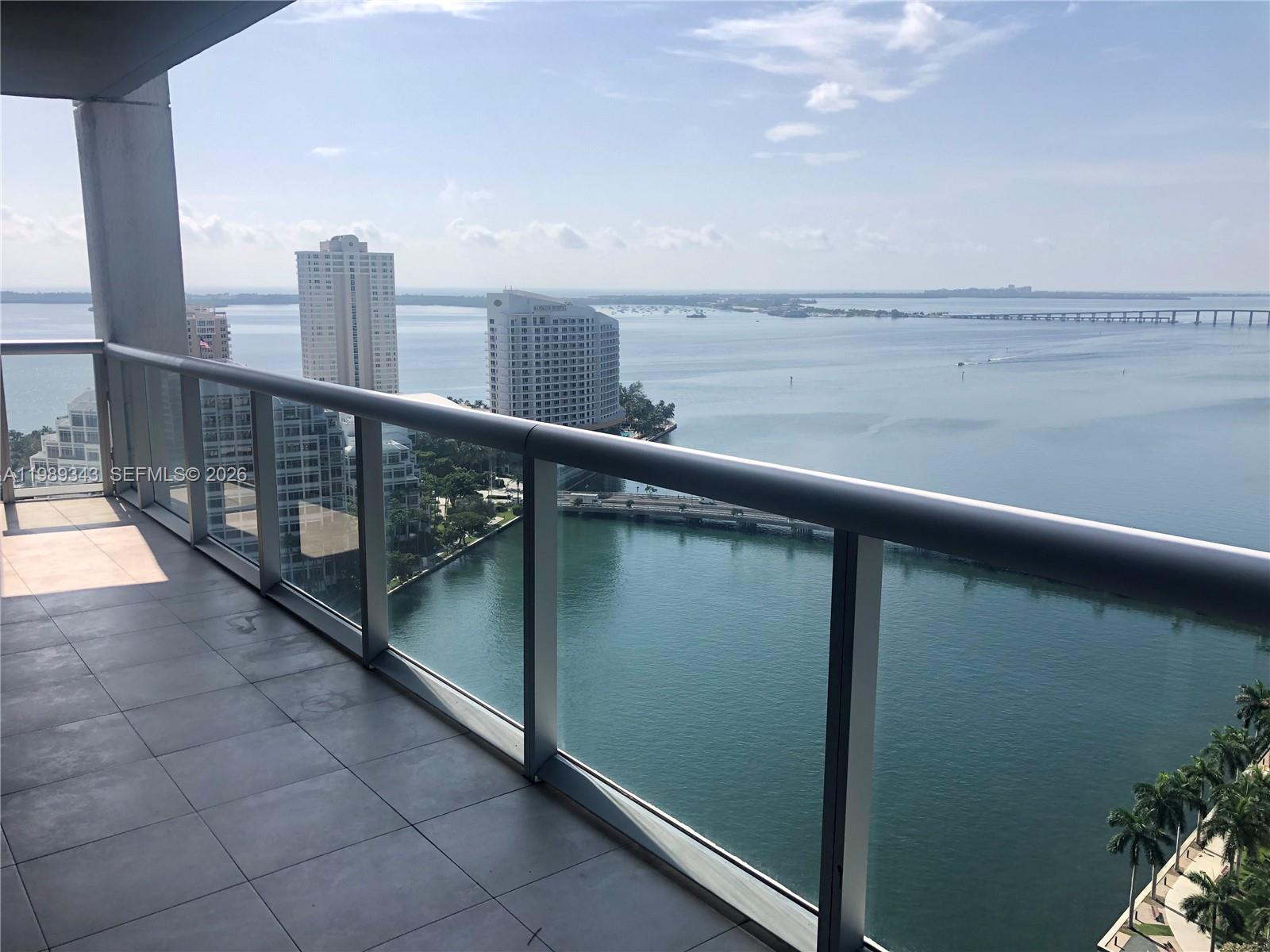 A high-rise balcony with a glass railing overlooks a bay, a bridge, and city buildings — 495 Brickell Ave # 2401, Miami FL 33131, MIAMI, FL