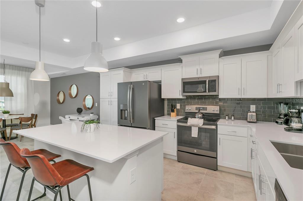 A modern kitchen features white cabinetry, a large quartz island, and stainless steel appliances — 3121 PARADOX CIRCLE UNIT 203, KISSIMMEE, FL