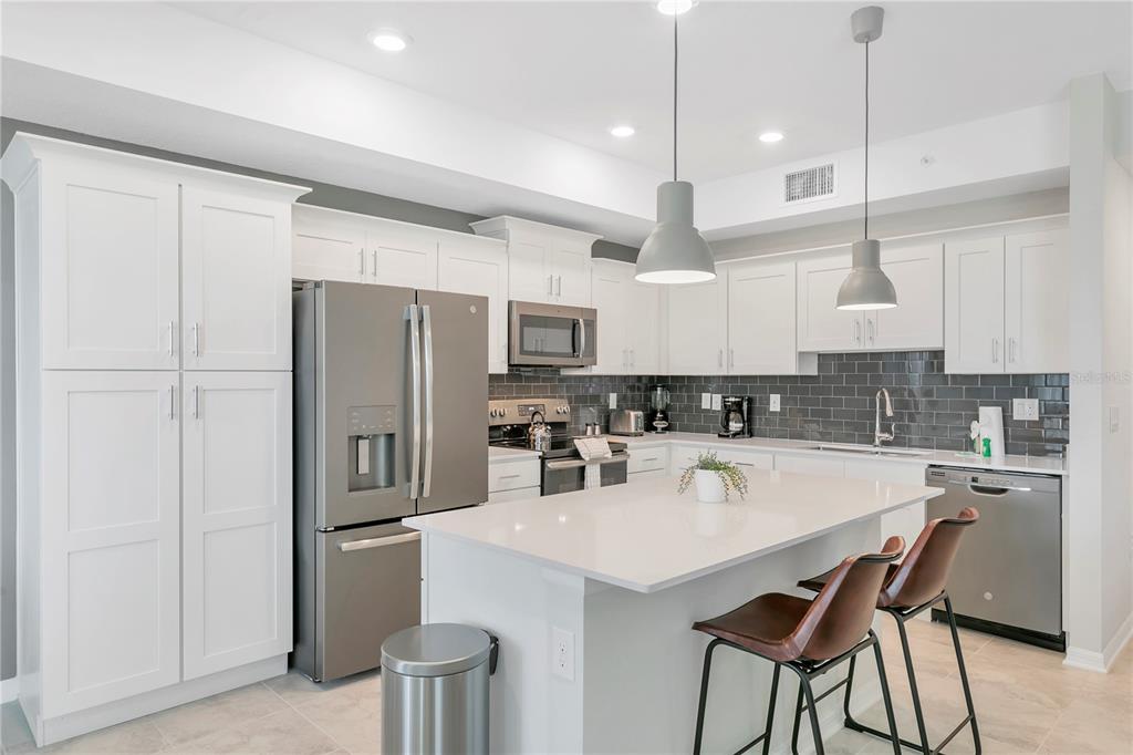 A modern kitchen features white cabinets, stainless steel appliances, a quartz island, and gray tile backsplash — 3121 PARADOX CIRCLE UNIT 203, KISSIMMEE, FL