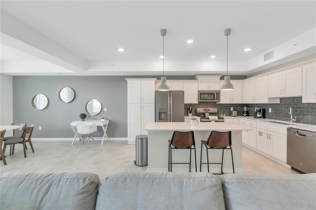 A modern kitchen features white cabinetry, a central island with bar stools, and gray walls — 3121 PARADOX CIRCLE UNIT 203, KISSIMMEE, FL