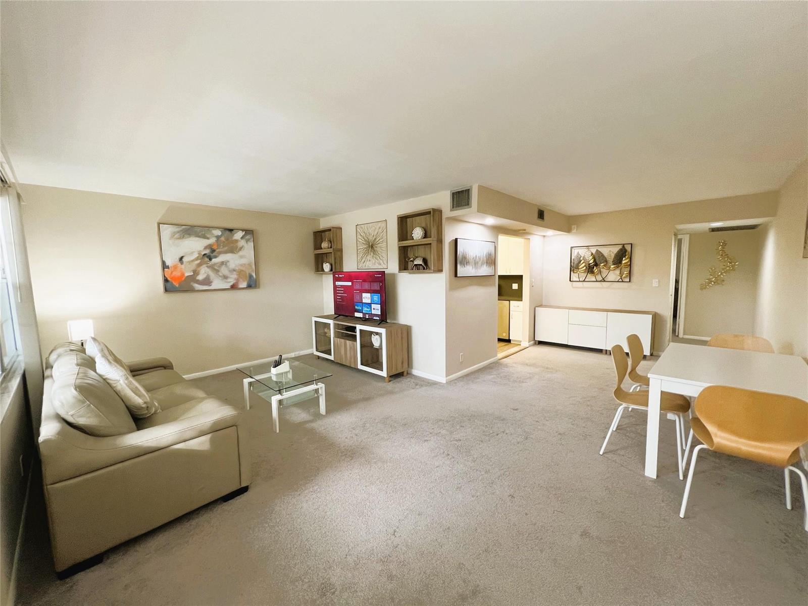A living room with beige carpet, a leather sofa, a television console, and dining area — 1902 Bermuda Circle # 2, Coconut Creek FL 33066, COCONUT CREEK, FL