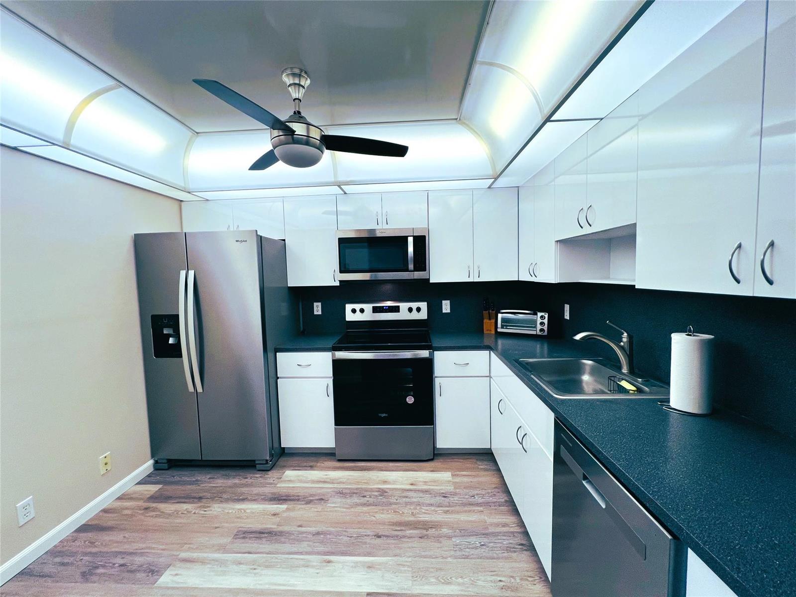 A kitchen features white cabinets, stainless steel appliances, dark countertops, and wood-look flooring — 1902 Bermuda Circle # 2, Coconut Creek FL 33066, COCONUT CREEK, FL