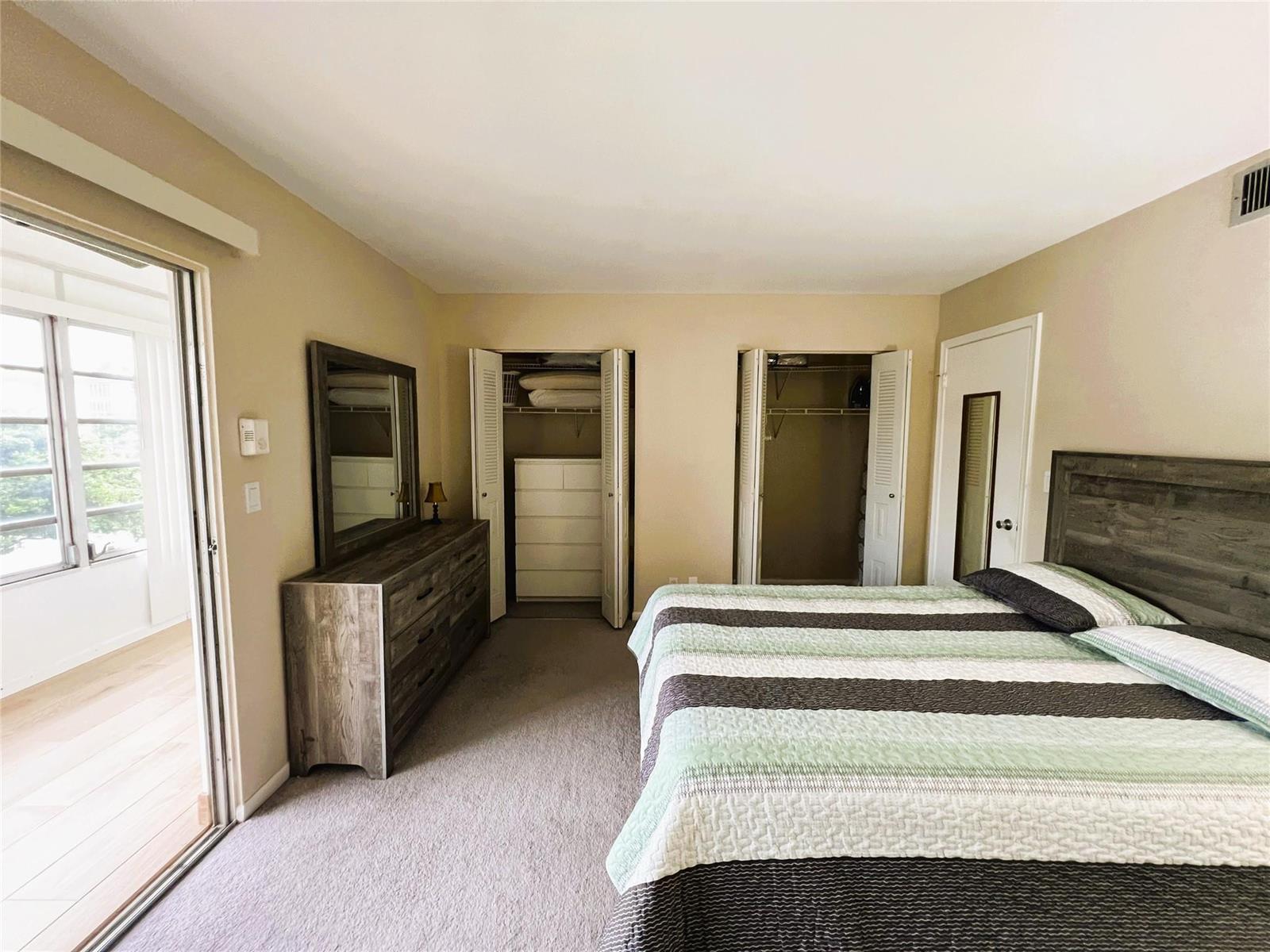 A bedroom features a bed, a dresser with a mirror, two closets, and a balcony door — 1902 Bermuda Circle # 2, Coconut Creek FL 33066, COCONUT CREEK, FL