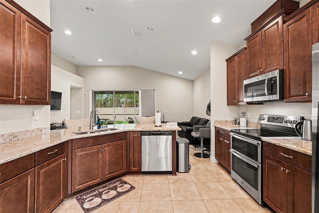 A kitchen with dark wood cabinets, granite countertops, stainless steel appliances, and tile flooring — 7907 SILVER CLOVER COURT, RIVERVIEW, FL