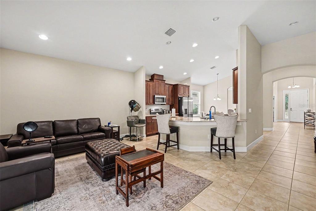 An open-concept living room and kitchen featuring dark leather furniture, tile flooring, and wood cabinetry — 7907 SILVER CLOVER COURT, RIVERVIEW, FL