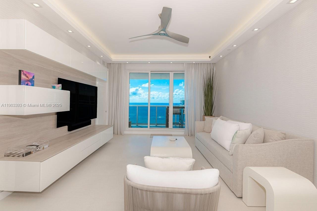 A modern living room features a large television, light-colored furniture, and a balcony overlooking the ocean — 2301 Collins Ave, Miami Beach FL 33139, MIAMI BEACH, FL
