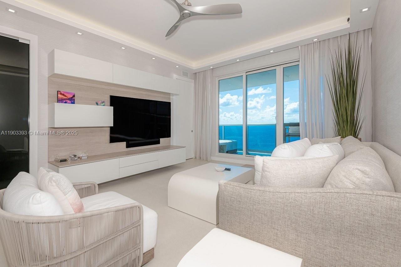 A modern living room features a large television, white cabinetry, and a balcony overlooking ocean — 2301 Collins Ave, Miami Beach FL 33139, MIAMI BEACH, FL