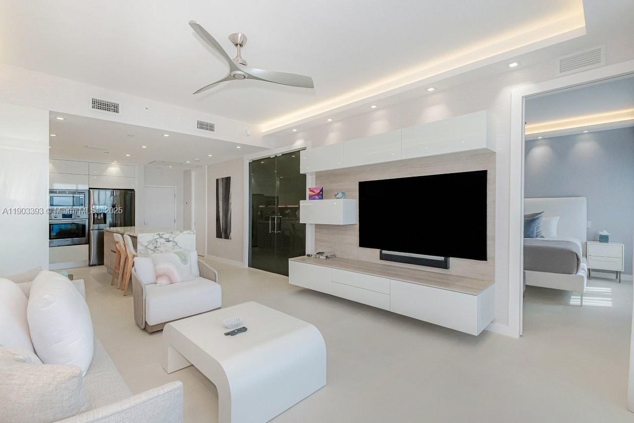 A modern living room features a large television, white cabinetry, and an adjacent kitchen area — 2301 Collins Ave, Miami Beach FL 33139, MIAMI BEACH, FL