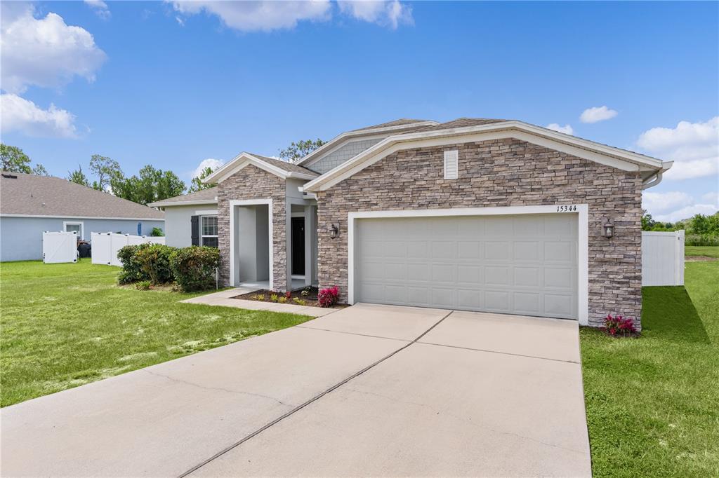 A single-story house with a stone veneer facade, a two-car garage, and a concrete driveway — 15344 WHITE TAIL LOOP, MASCOTTE, FL