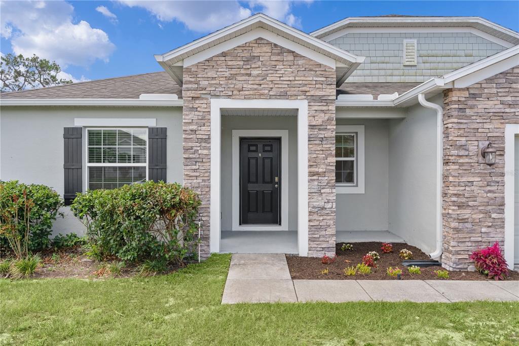 The exterior of a house features a stone-accented entryway, a black front door, and landscaping — 15344 WHITE TAIL LOOP, MASCOTTE, FL