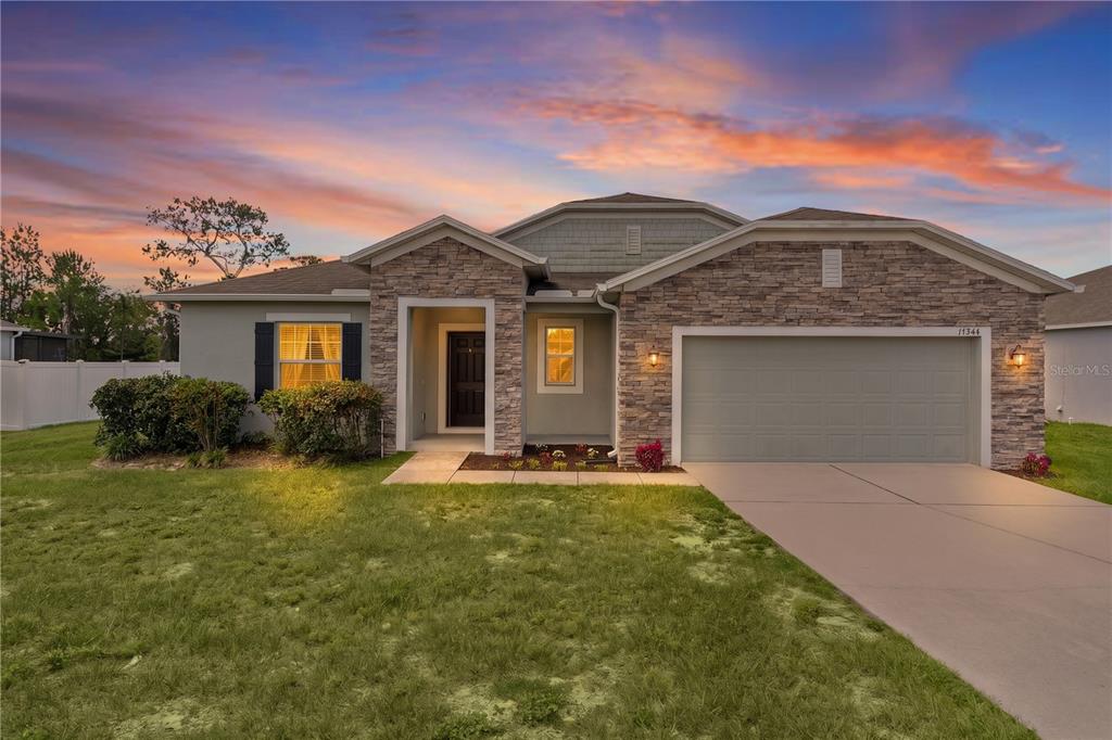 A single-story suburban house with a stone facade, a two-car garage, and a grassy lawn — 15344 WHITE TAIL LOOP, MASCOTTE, FL