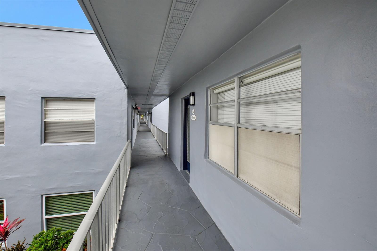 An exterior walkway with gray flooring and walls leads past apartment doors and windows — 126 Burgundy # C, Delray Beach FL 33484, DELRAY BEACH, FL