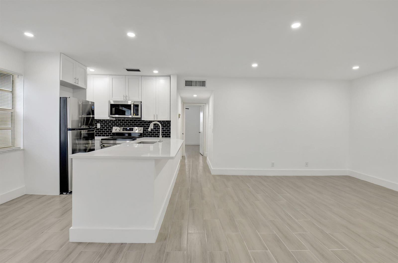 A modern kitchen with white cabinets, black subway tile backsplash, and a white island — 126 Burgundy # C, Delray Beach FL 33484, DELRAY BEACH, FL