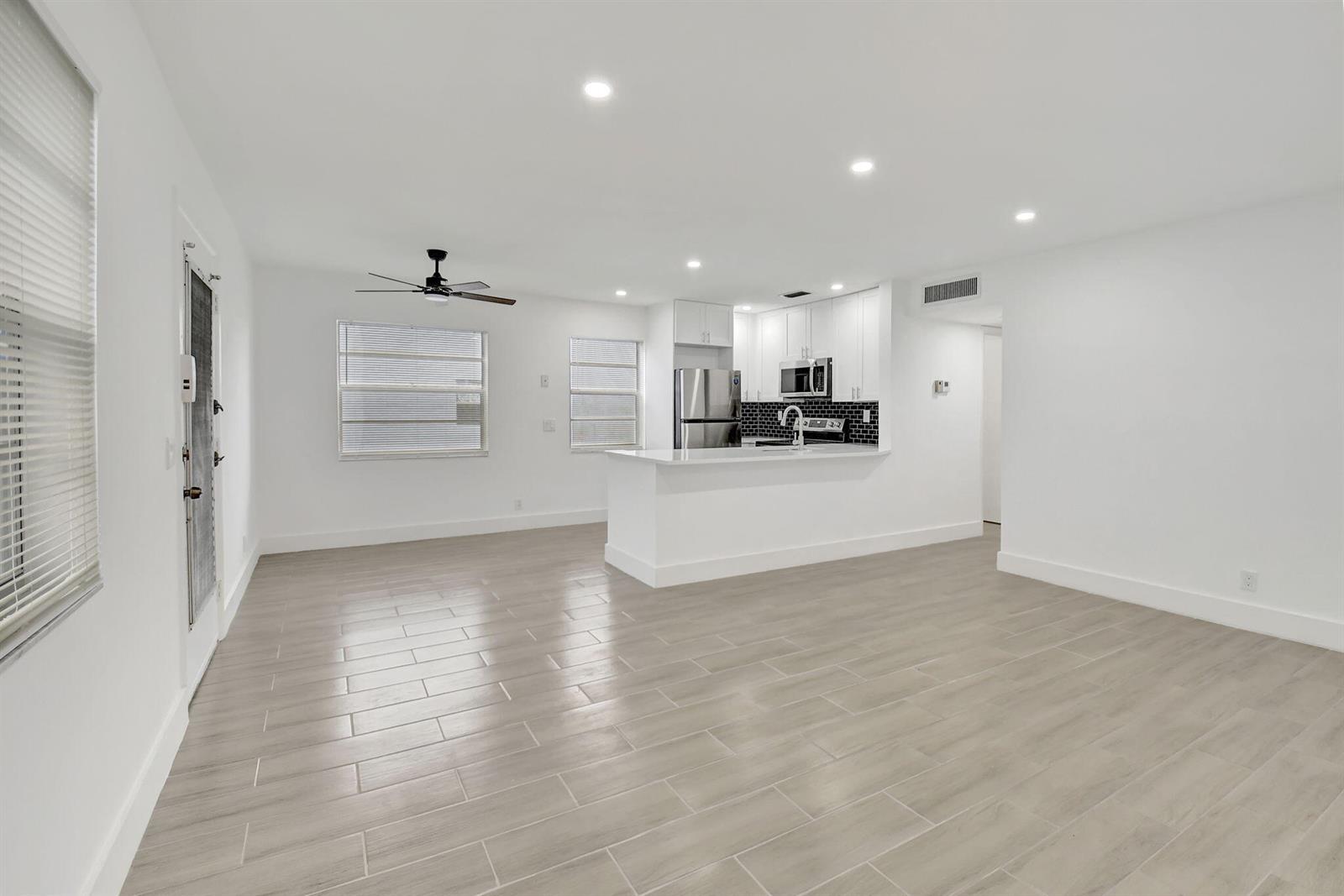 A bright, open-concept living area features light wood-look tile flooring and a modern kitchen — 126 Burgundy # C, Delray Beach FL 33484, DELRAY BEACH, FL