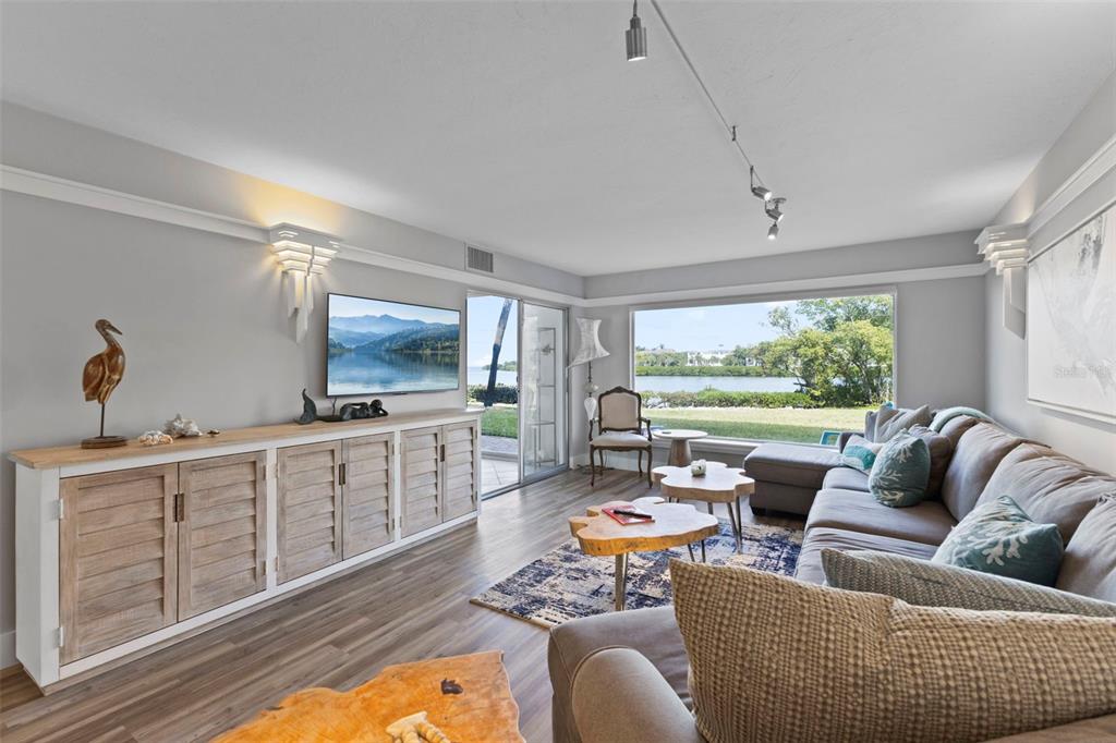 A living room features a large sectional sofa, wooden media console, and waterfront window views — 3330 GULF OF MEXICO DRIVE UNIT 104D, LONGBOAT KEY, FL