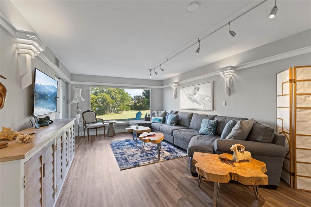 A living room features a gray sectional sofa, wood-topped coffee tables, and a large window — 3330 GULF OF MEXICO DRIVE UNIT 104D, LONGBOAT KEY, FL