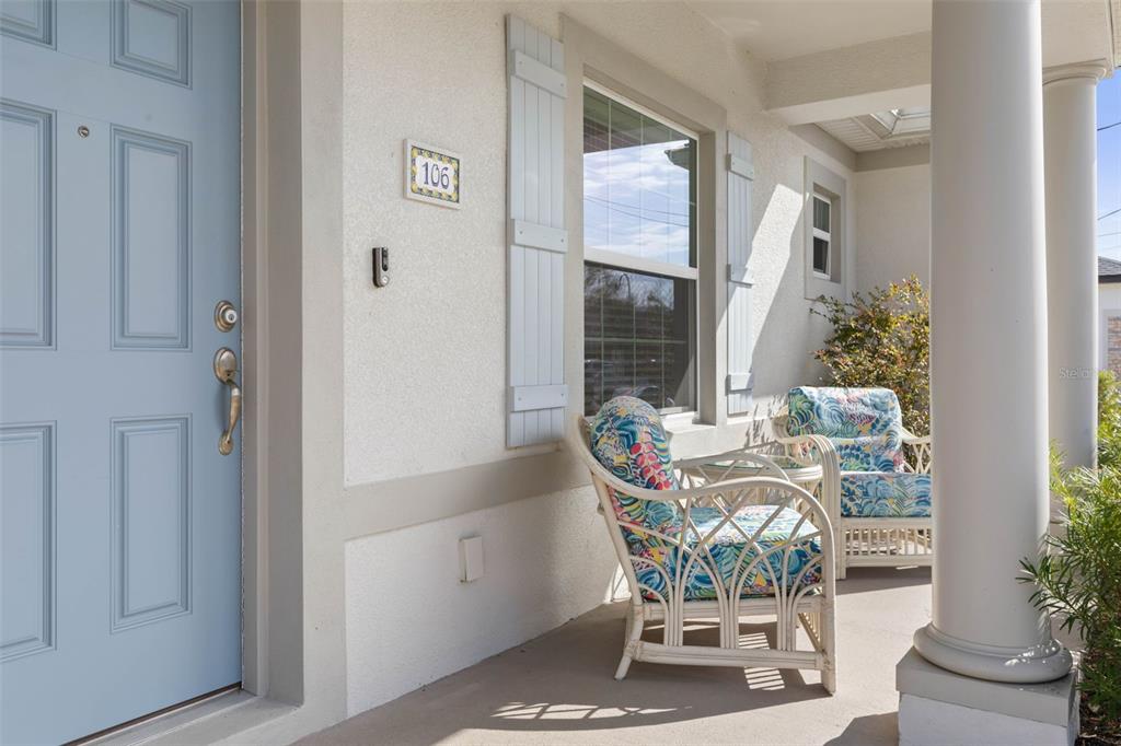 A light blue front door and two wicker chairs sit on a covered front porch — 106 BIRCHWOOD DRIVE, PALM COAST, FL