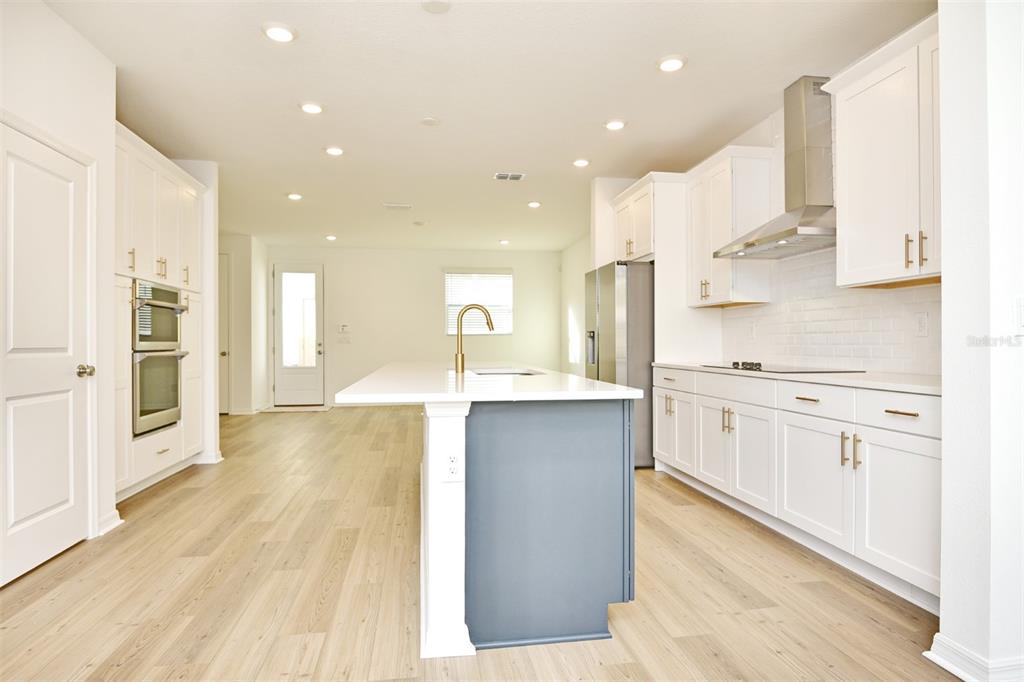 A modern kitchen features white cabinetry, a blue island, stainless steel appliances, and wood flooring — 2948 VOYAGER AVENUE, ST CLOUD, FL