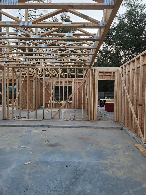 An unfinished room with exposed wooden wall studs and roof trusses over a concrete floor — 228 DAWN AVENUE, INTERLACHEN, FL