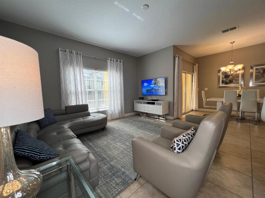A living room features a grey sectional sofa, two armchairs, a television, and tile flooring — 2937 BANANA PALM DRIVE, KISSIMMEE, FL