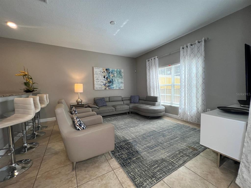 A living room features a grey sectional sofa, two armchairs, a rug, and bar stools — 2937 BANANA PALM DRIVE, KISSIMMEE, FL