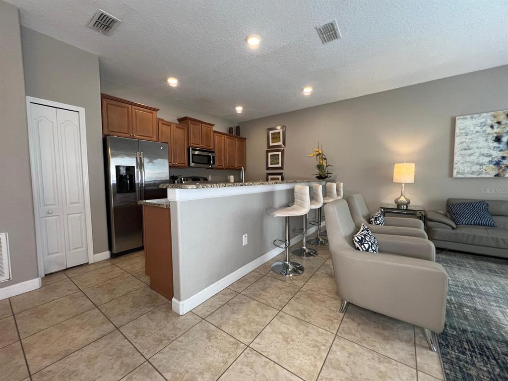 A kitchen with wood cabinets and stainless steel appliances overlooks a living area with chairs — 2937 BANANA PALM DRIVE, KISSIMMEE, FL
